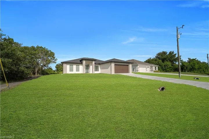 Modern exterior with a two-car garage, concrete driveway, expansive front lawn, and mature perimeter trees