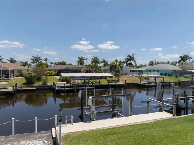 View of dock with a water view, a residential view, boat lift, and a lawn