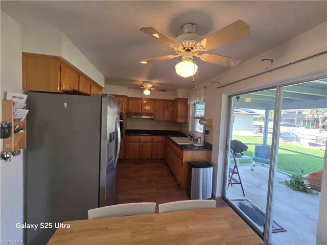 Kitchen with black stovetop, stainless steel fridge with ice dispenser, under cabinet range hood, a sink, and dark countertops