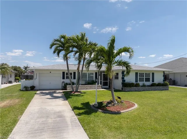 Single story home featuring a front yard, central AC unit, a garage, stucco siding, and driveway