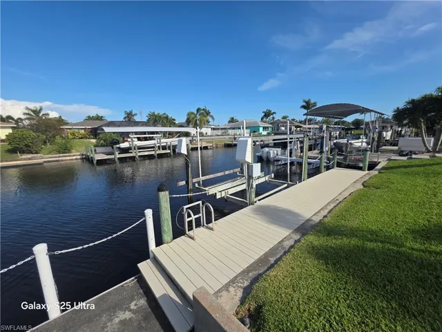 View of dock with a water view, boat lift, and a yard
