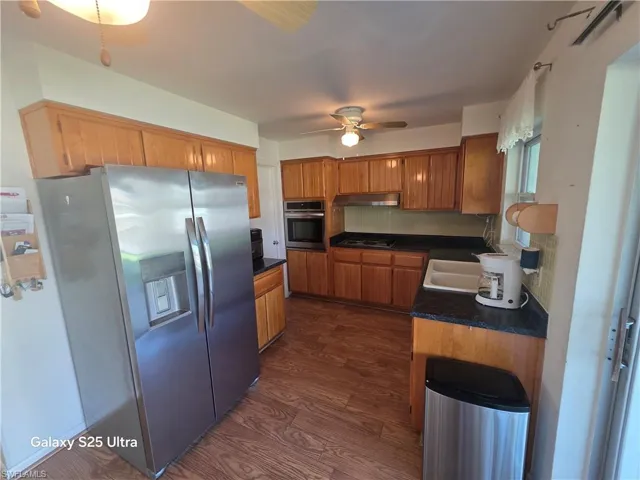 Kitchen featuring under cabinet range hood, backsplash, dark countertops, dark wood-style floors, and appliances with stainless steel finishes
