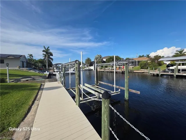 View of dock featuring a lawn, a water view, boat lift, and a residential view