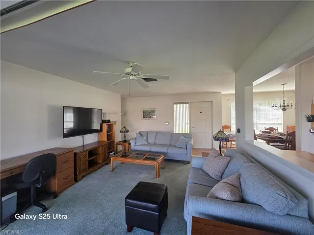 Living area with ceiling fan with notable chandelier and carpet