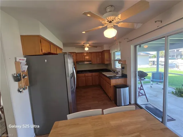 Kitchen featuring stainless steel fridge with ice dispenser, a sink, dark countertops, a ceiling fan, and brown cabinets