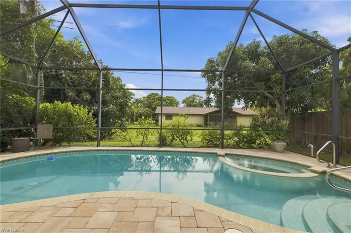 Screen-enclosed pool area featuring a built-in spa, paver patio, and lawn space