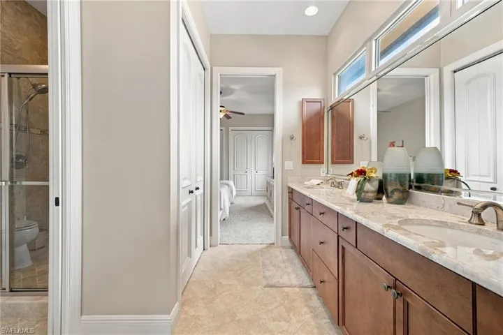 Double vanity with stone-look countertop, wood cabinetry, large wall-to-wall mirror, and glass-enclosed shower with tile surround