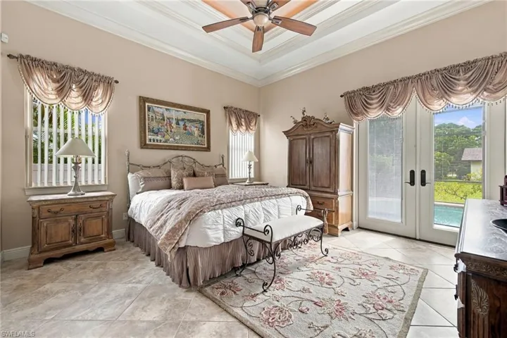 Tray ceiling, ceiling fan, and large-format tile flooring, featuring multiple windows and glass-paned double doors