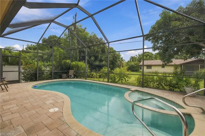 Screened lanai featuring a paver deck, a kidney-shaped pool, and an integrated spa with metal handrails