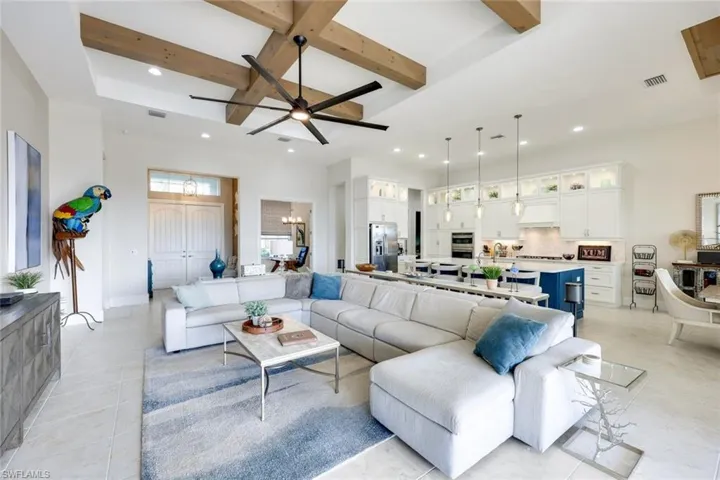 Tiled living room featuring ceiling fan with notable chandelier, beam ceiling, and coffered ceiling