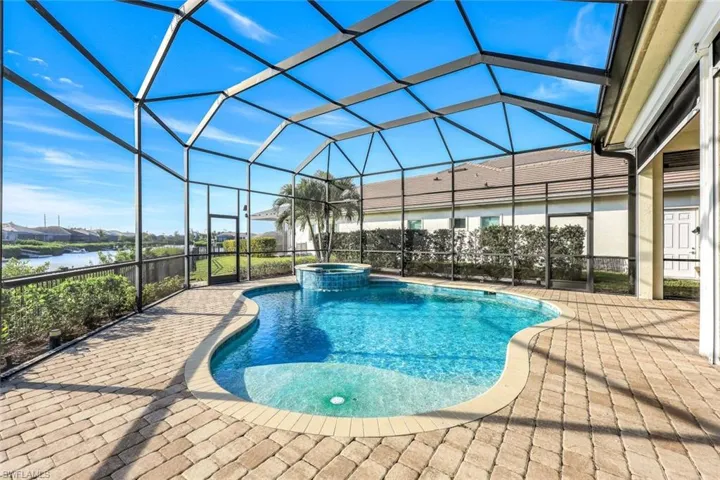 View of pool with an in ground hot tub, a patio, a water view, and glass enclosure