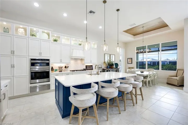 Kitchen featuring a kitchen bar, premium range hood, a tray ceiling, pendant lighting, and an island with sink