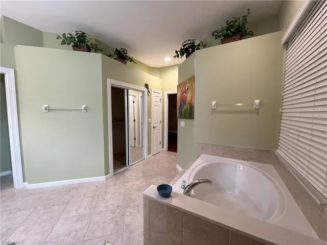 Spacious bathroom featuring an oval soaking tub with tiled surround, light-toned ceramic tile flooring, and a mirrored closet door