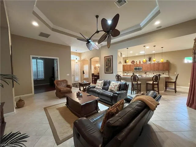 Spacious living area featuring tile flooring, a tray ceiling with a ceiling fan, and recessed lighting