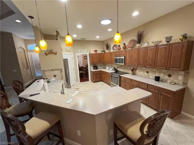 Expansive kitchen featuring a large island with sink, wood-finish cabinetry, tile flooring, and a tiled backsplash