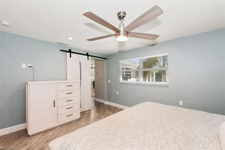 Bedroom featuring a barn door, light wood-type flooring, a ceiling fan, and recessed lighting