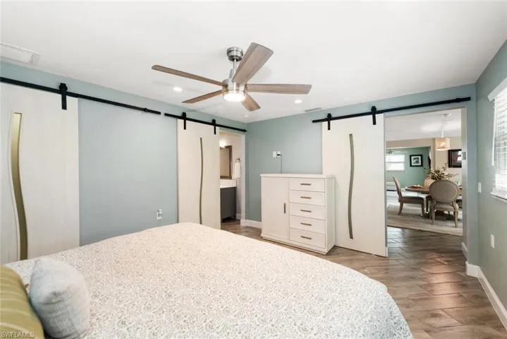 Bedroom with a barn door, light wood finished floors, ceiling fan, and ensuite bath