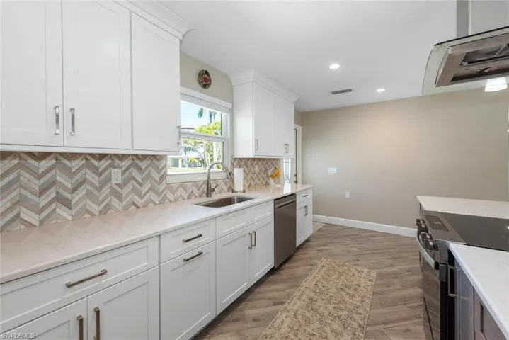 Kitchen featuring electric range, white cabinets, ventilation hood, light stone counters, and decorative backsplash