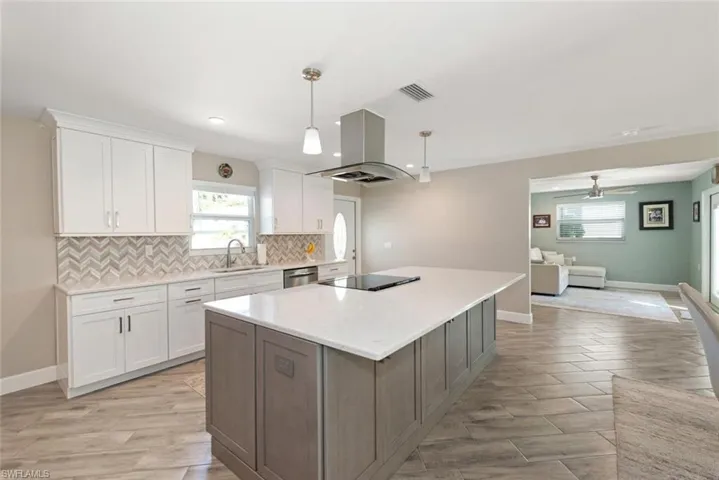 Dual tone kitchen featuring island range hood, two tone cabinetry, decorative light fixtures, wood finish floors, and light stone countertops