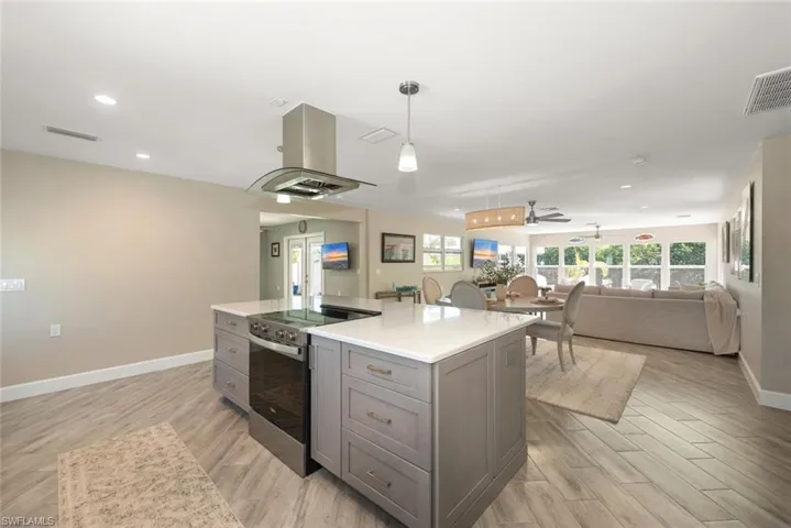 Kitchen with stainless steel range with electric cooktop, island range hood, light wood finished floors, and a kitchen island