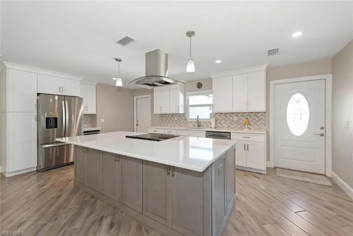 Kitchen with two tone cabinetry, stainless steel appliances, island exhaust hood, a center island, and pendant lighting