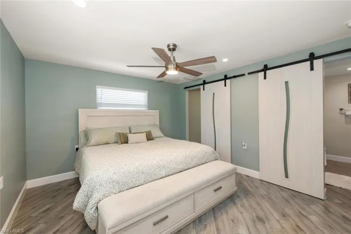 Bedroom with a barn door, light wood finished floors, a ceiling fan, recessed lighting, and ensuite bathroom