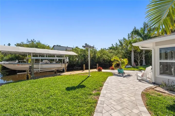 View of green lawn with boat lift, a boat dock, and a water view