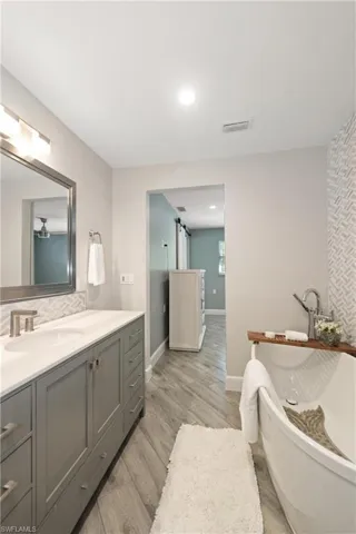 Full bath with vanity, a freestanding tub, light wood-type flooring, recessed lighting, and decorative backsplash
