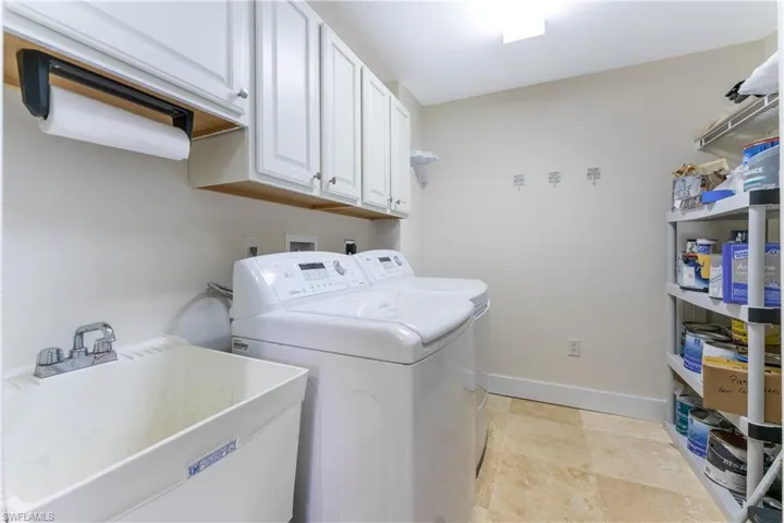 Clothes washing area with cabinets, independent washer and dryer, light tile flooring, sink, and hookup for an electric dryer