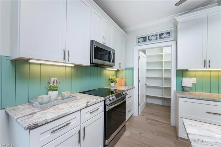 Kitchen featuring crown molding, white cabinetry, light hardwood / wood-style flooring, stainless steel appliances, and light stone counters