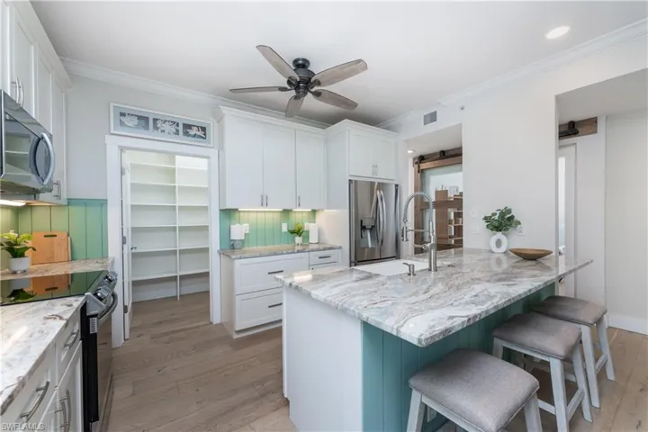 Kitchen with ceiling fan, light wood-type flooring, white cabinetry, and appliances with stainless steel finishes