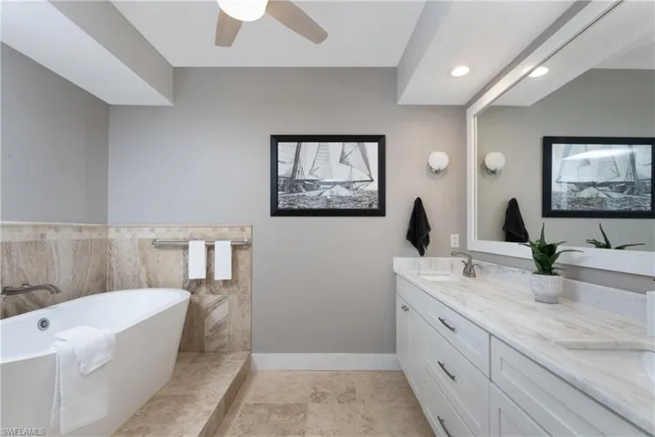 Bathroom with a bath, double vanity, tile floors, tile walls, and ceiling fan