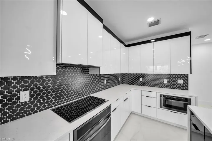 Kitchen featuring tasteful backsplash, light stone countertops, white cabinets, and stainless steel appliances