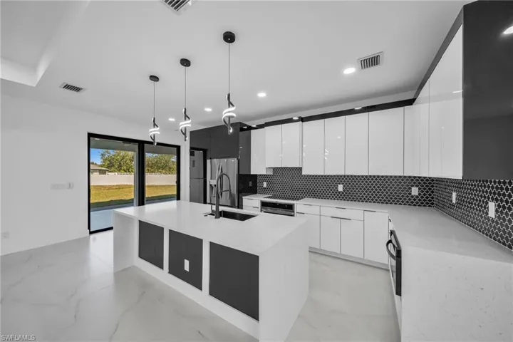 Kitchen with white cabinetry, sink, hanging light fixtures, backsplash, and a center island with sink