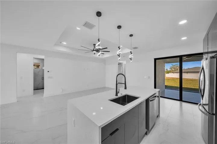 Kitchen with stainless steel appliances, ceiling fan, sink, pendant lighting, and an island with sink