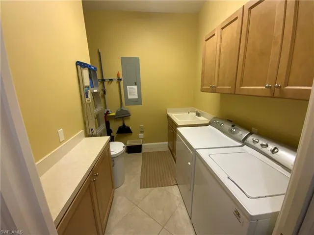 Laundry room with washing machine and clothes dryer, electric panel, cabinet space, and light tile patterned floors