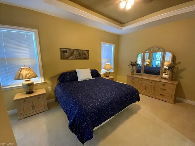 Bedroom with light colored carpet, a raised ceiling, and ceiling fan