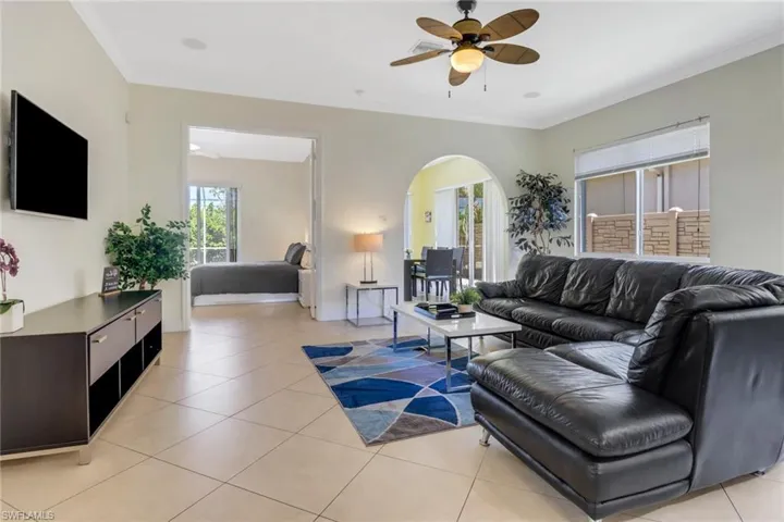 Living room with ceiling fan, light tile patterned floors, and crown molding