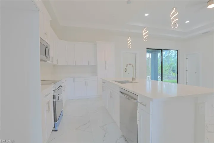 Kitchen featuring stainless steel appliances, a raised ceiling, light marble finish flooring, a center island with sink, and white cabinets