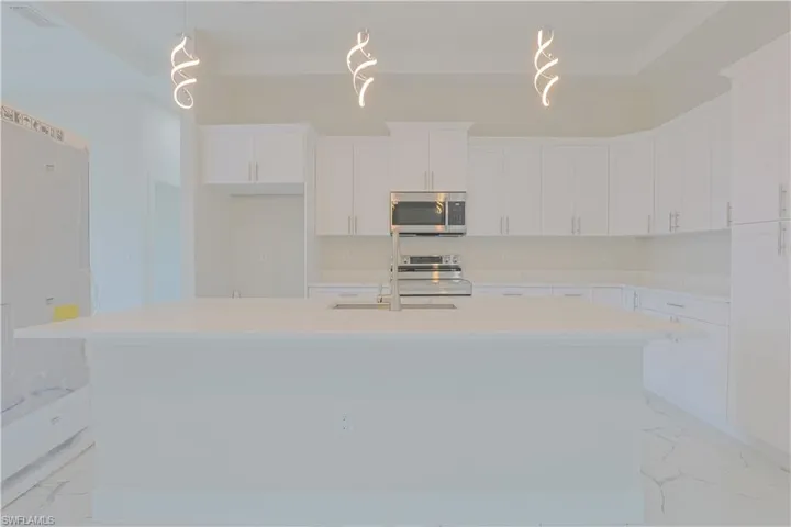 Kitchen featuring stainless steel microwave, light marble finish floors, electric range, and an island with sink