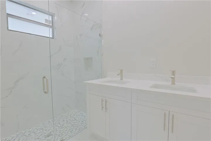 Full bath with a marble finish shower and double vanity
