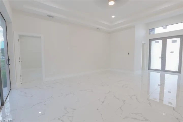 Unfurnished room featuring a tray ceiling, french doors, recessed lighting, light marble finish flooring, and ceiling fan