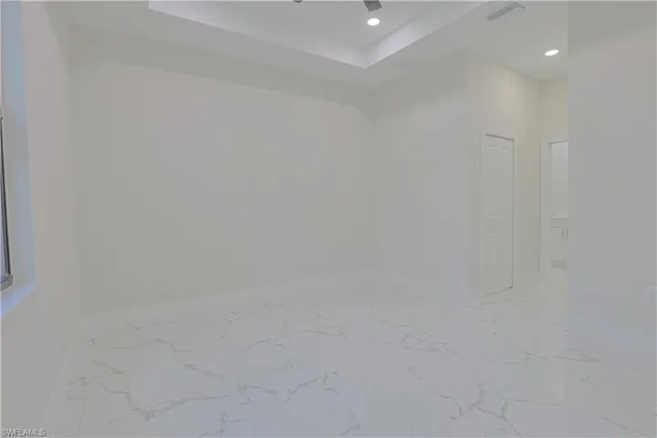 Unfurnished room featuring recessed lighting, light marble finish floors, and a raised ceiling