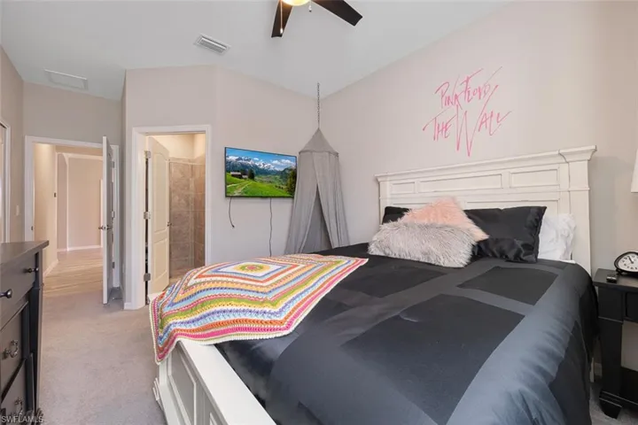 Carpeted bedroom featuring ceiling fan and ensuite bath