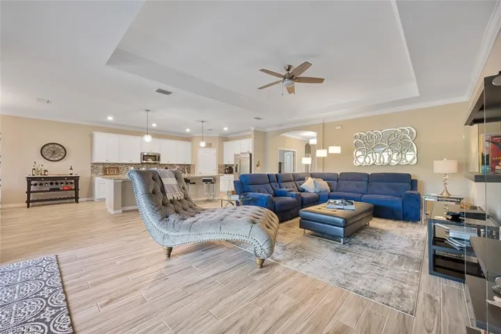 Living room with a raised ceiling, ceiling fan, and ornamental molding