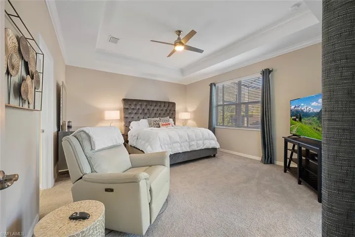 Bedroom featuring light carpet, ceiling fan, ornamental molding, and a raised ceiling