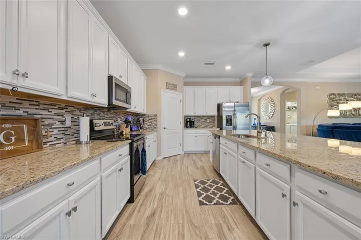 Kitchen featuring hanging light fixtures, crown molding, stainless steel appliances, and white cabinetry