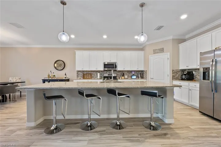 Kitchen with stainless steel appliances, white cabinetry, hanging light fixtures, and an island with sink