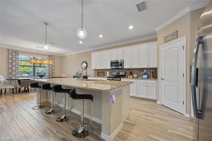 Kitchen with appliances with stainless steel finishes, pendant lighting, white cabinets, and a center island with sink