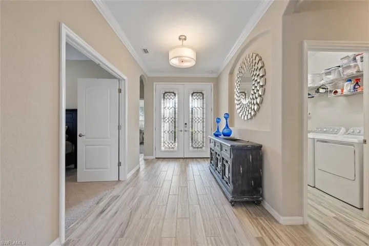 Foyer featuring french doors, crown molding, independent washer and dryer, and light wood-type flooring